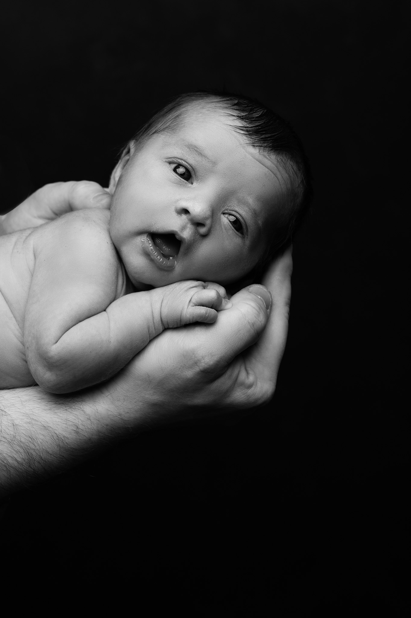bébé dans les bras de son papa sur fond noir qui sourit